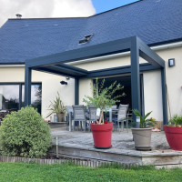 Pergola bioclimatique anthracite adossée, lames rétractables sur terrasse carrelée et salon de jardin