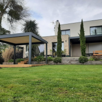 Pergola bioclimatique anthracite sur terrasse bois devant maison moderne pierre et enduit blanc