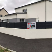 Clôture brise-vue lames anthracite sur muret blanc devant maison contemporaine blanche et bandeau gris foncé