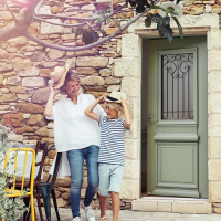 Porte d'entrée vert olive, imposte grille fer forgée noire dans mur pierres rustiques ensoleillé
