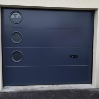 Porte sectionnelle gris anthracite, trois hublots circulaires alignés à gauche, poignée noire