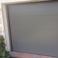Porte sectionnelle gris anthracite, quatre panneaux lisses, seuil briquettes et hortensias à gauche