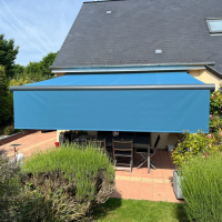 Store banne bleu déployé avec lambrequin vertical au-dessus terrasse pavée, table et chaises grises