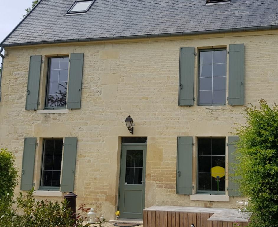 Façade pierre beige, fenêtres et porte avec volets battants vert olive, toit ardoise grise