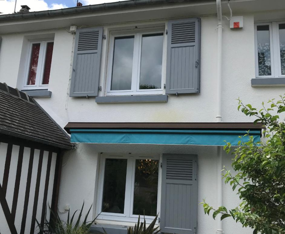 Façade blanche, fenêtres PVC blanches, volets battants gris ouverts et store banne bleu turquoise