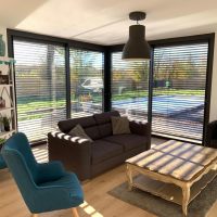 Salon avec baies vitrées, brise-soleil orientables noirs entrouverts, ombres rayées sur le sol