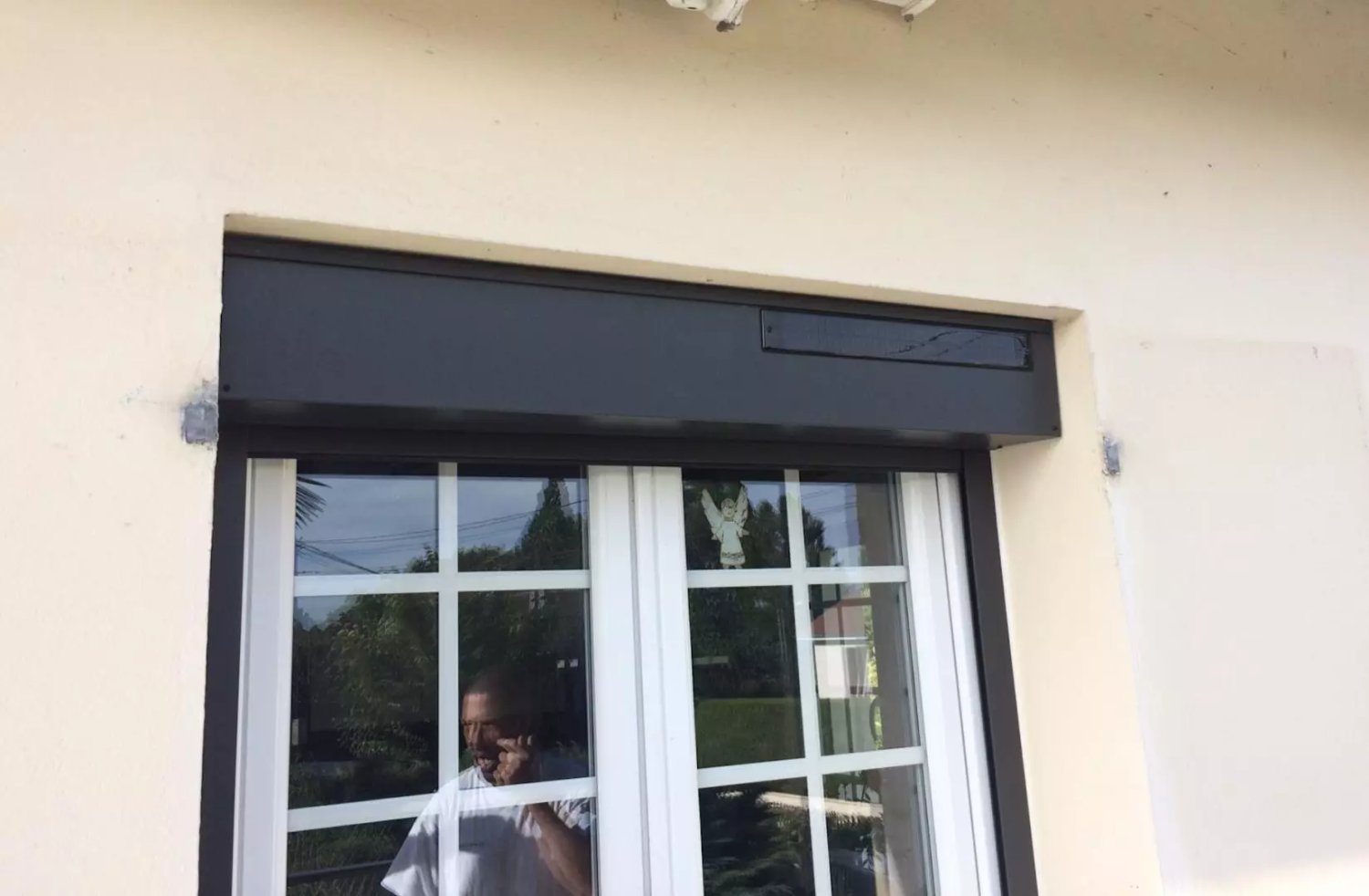Coffre volet roulant anthracite avec panneau solaire sur fenêtre blanche petits bois, mur crépi crème