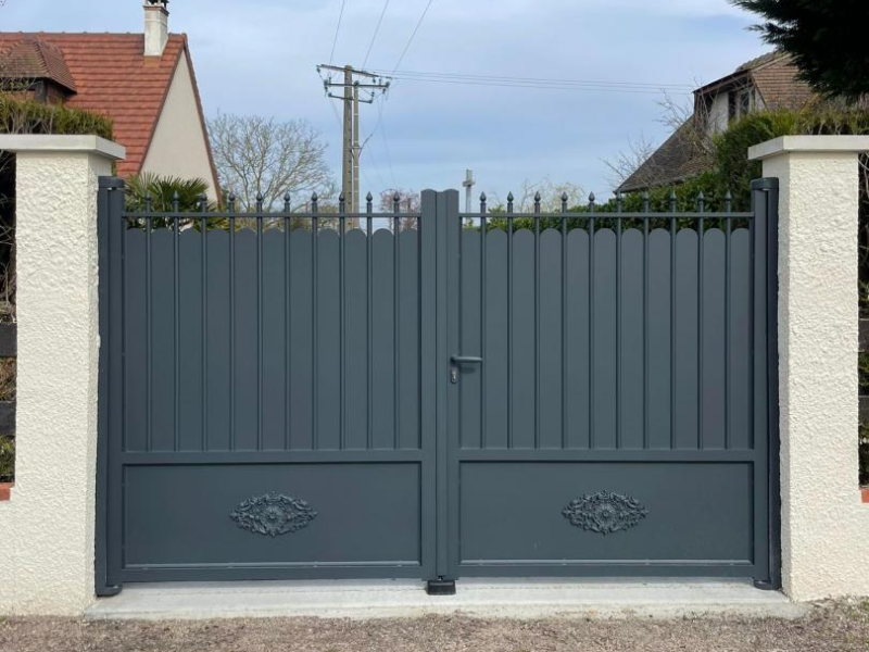 Portail battant anthracite à haut festonné et bas plein décoré, entre piliers blancs