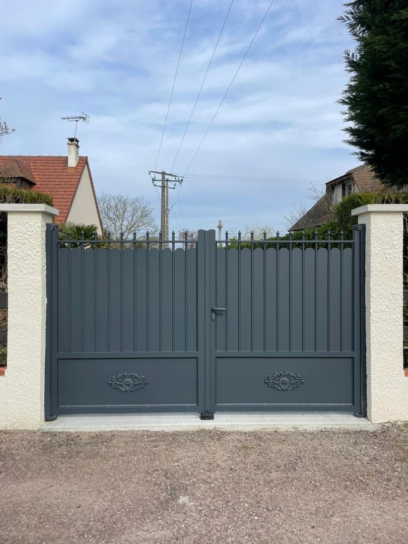 Portail battant anthracite à haut festonné et bas plein décoré, entre piliers blancs