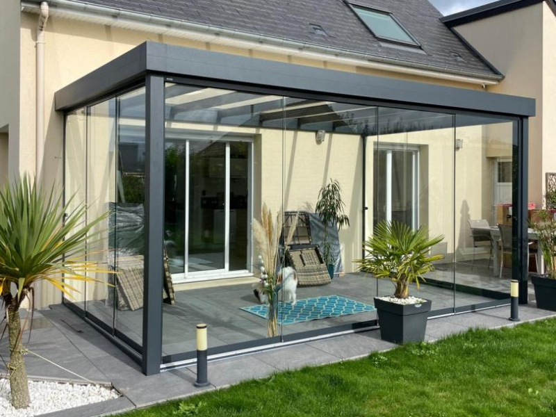 Véranda aluminium anthracite vitrée sur terrasse carrelée devant maison crème