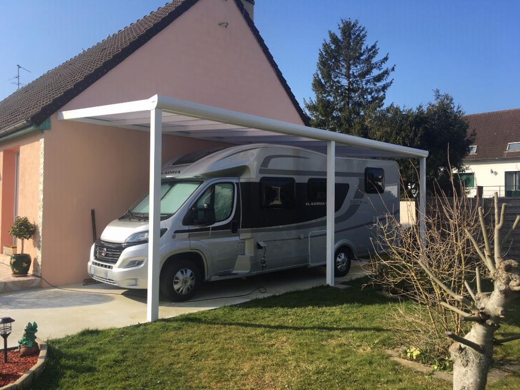 Carport blanc adossé à une maison saumon, camping-car argenté dessous