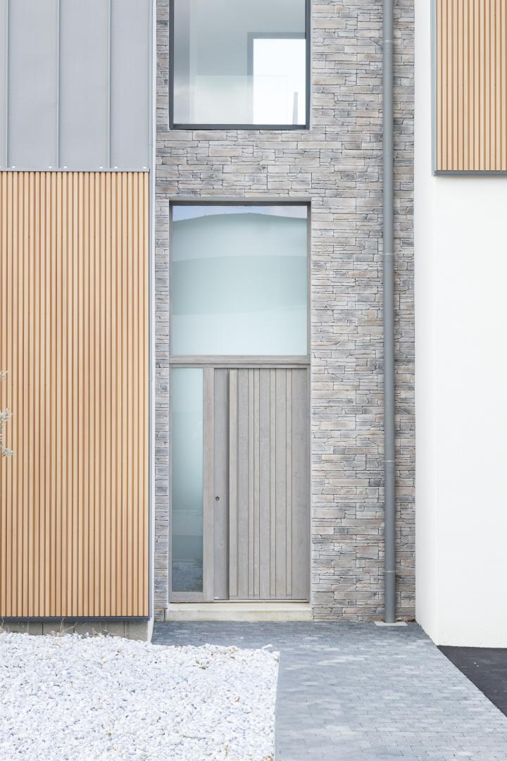 Porte d'entrée bois gris clair avec vitrage latéral et imposte, mur pierre