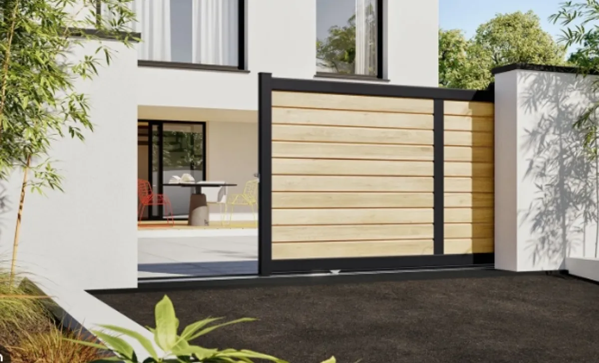 Portail coulissant à lames aspect bois clair et cadre noir devant maison blanche