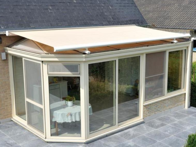 Store de véranda à toile beige sur extension vitrée crème et terrasse grise