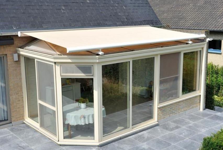Store de véranda à toile beige sur extension vitrée crème et terrasse grise
