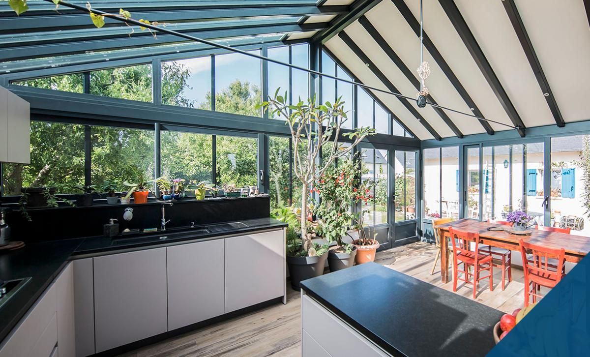 Véranda aluminium anthracite avec cuisine et table bois, vue sur jardin