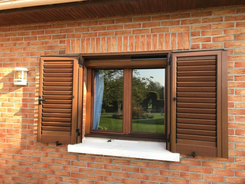 Fenêtre et volets battants à persiennes aspect bois marron sur façade en briques rouges