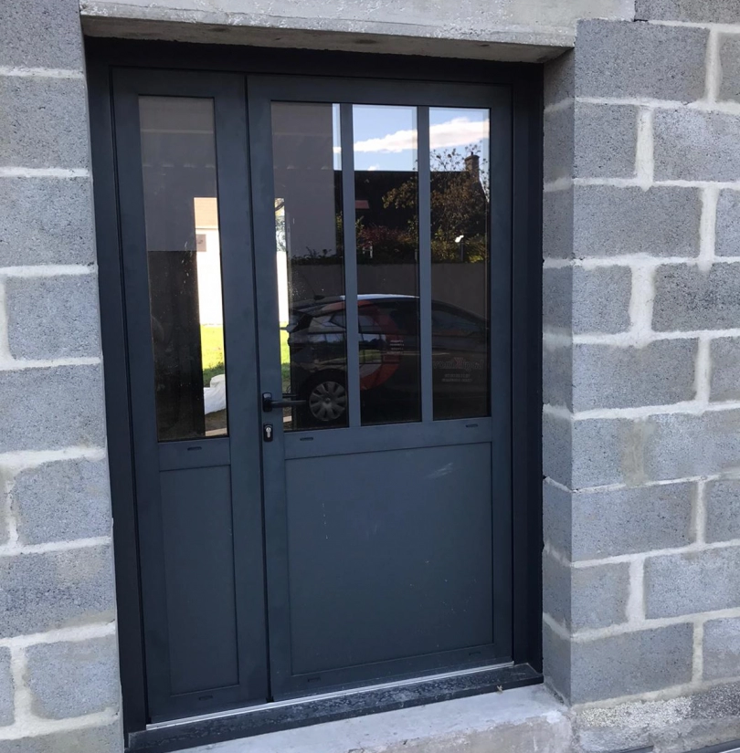 Porte d'entrée gris anthracite vitrée style atelier posée dans mur parpaings chantier