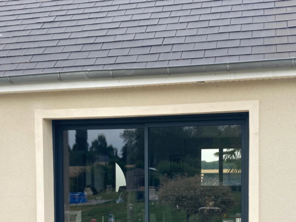 Baie coulissante alu anthracite sur façade enduit beige, toiture ardoises grises