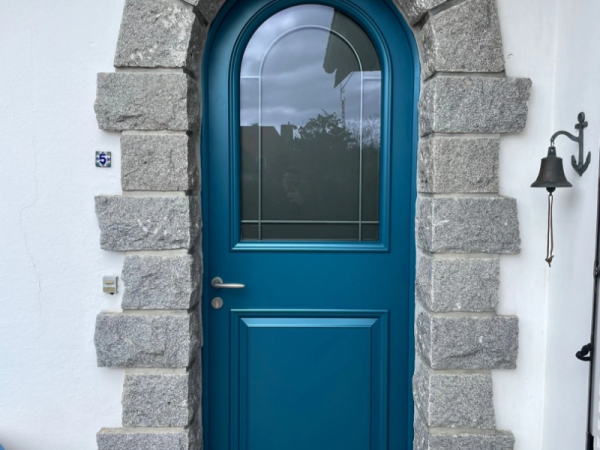 Porte d'entrée cintrée bleu canard, vitrage décoratif, encadrée d'une arche en pierre grise