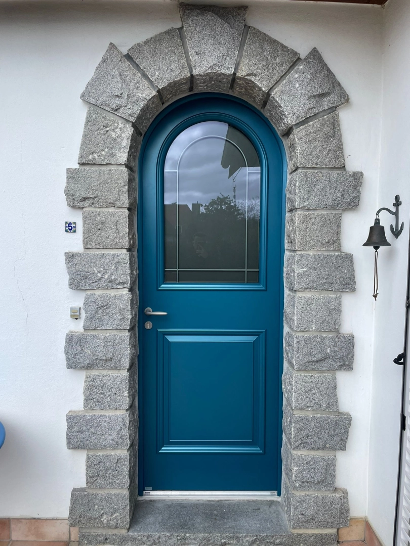 Porte d'entrée cintrée bleu canard, vitrage décoratif, encadrée d'une arche en pierre grise