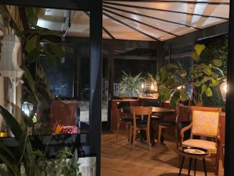 Véranda éclairée la nuit, toit rayonnant, salle à manger bois et plantes vertes