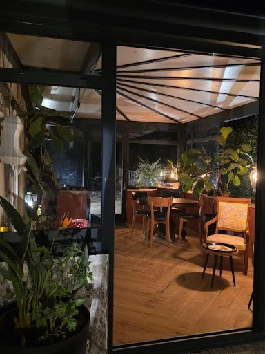 Véranda éclairée la nuit, toit rayonnant, salle à manger bois et plantes vertes
