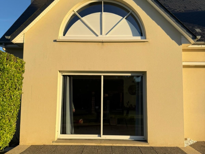 Baie vitrée blanche et fenêtre demi-lune à volet rayonnant sur façade enduit beige