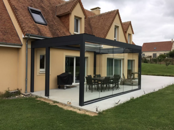 Véranda alu noir toit plat, parois vitrées coulissantes, dalle béton, salon et barbecue