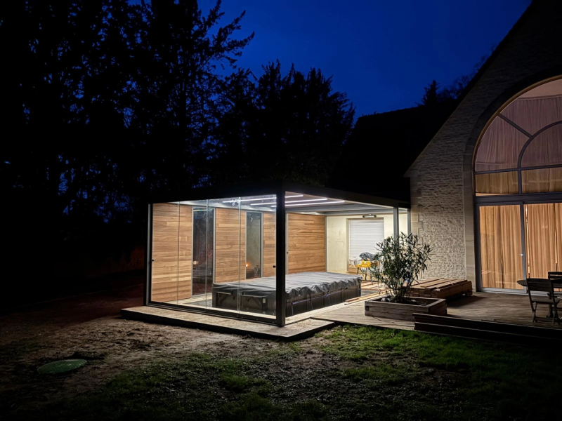Pergola vitrée anthracite de nuit, bardage bois intérieur, spa couvert et terrasse bois