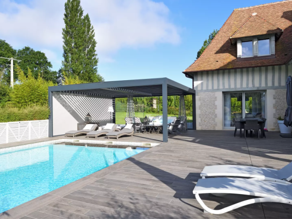 Pergola bioclimatique grise lames orientables, store blanc, terrasse et piscine bleue