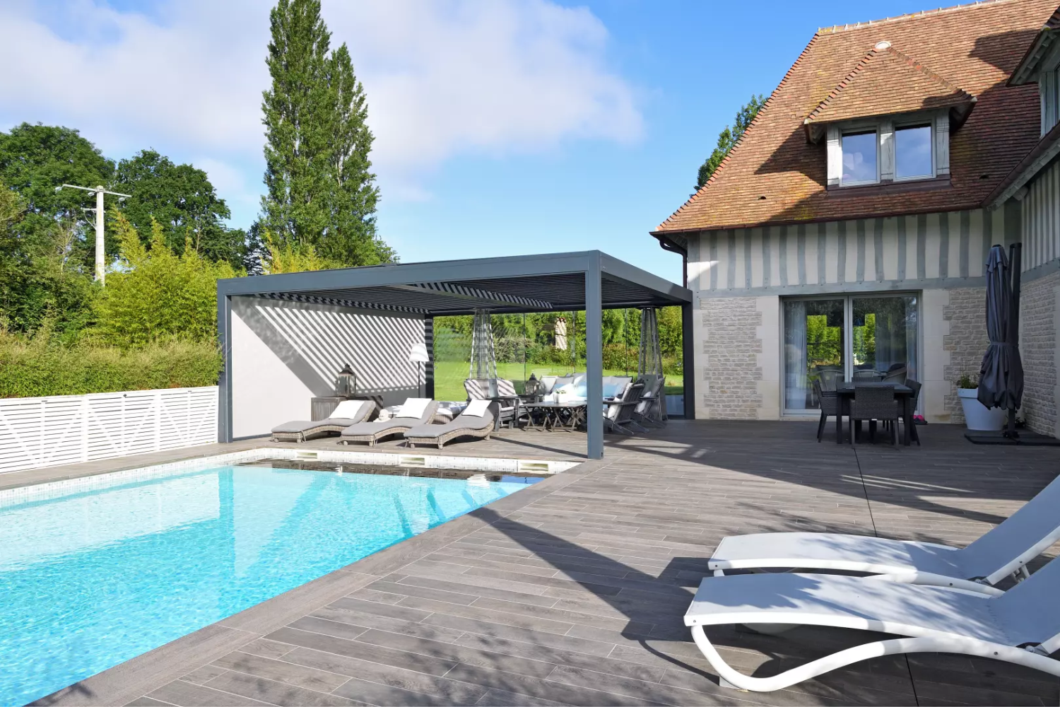 Pergola bioclimatique grise lames orientables, store blanc, terrasse et piscine bleue