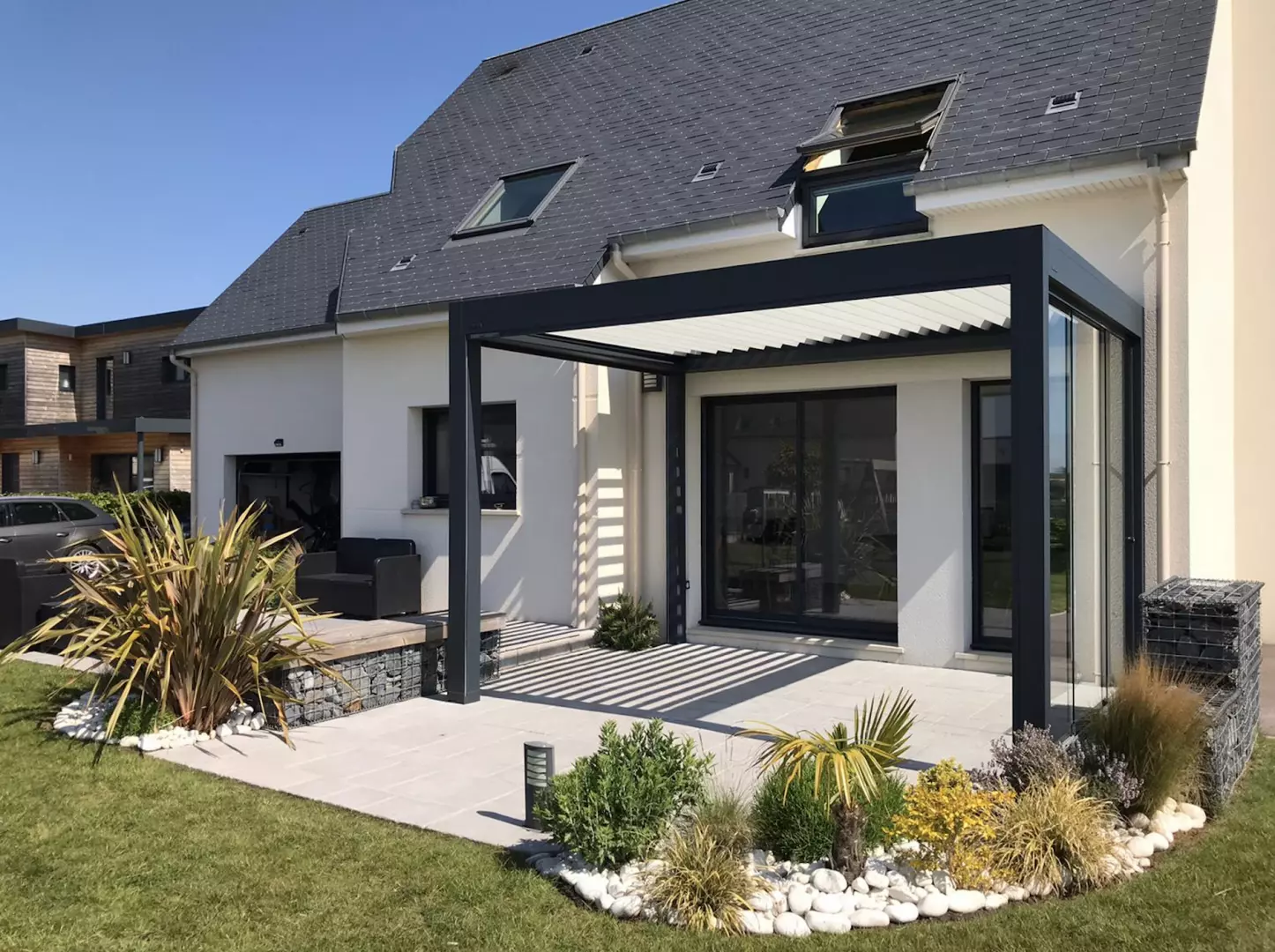 Pergola bioclimatique anthracite, lames claires, paroi vitrée coulissante, terrasse dalles grises