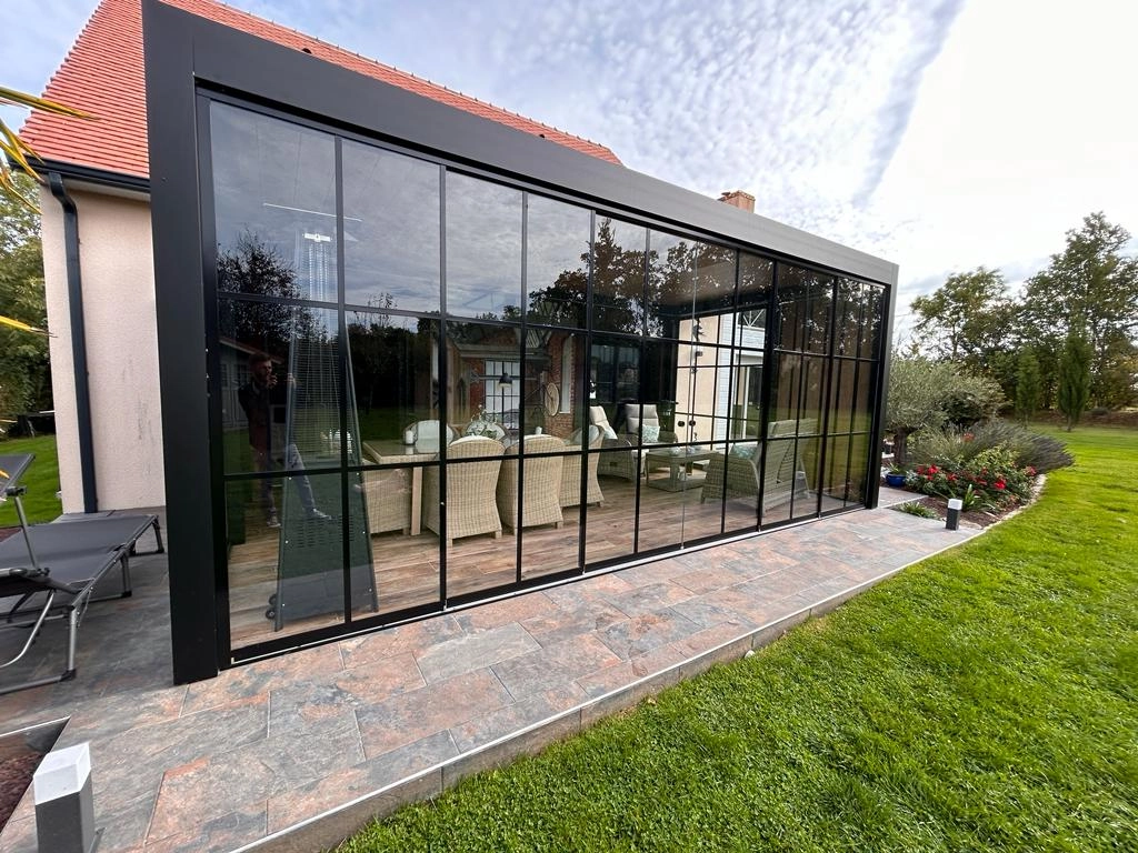 Pergola alu noir verrière vitrée quadrillée, terrasse dalles, maison tuiles rouges