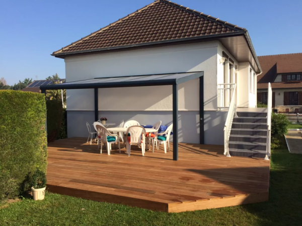 Terrasse bois clair en L, pergola adossée alu anthracite toit translucide, façade blanche