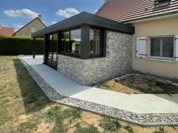 Extension alu anthracite toit plat, parement pierre et chemin béton graviers