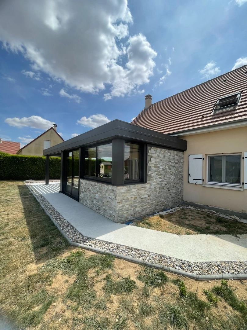 Extension alu anthracite toit plat, parement pierre et chemin béton graviers