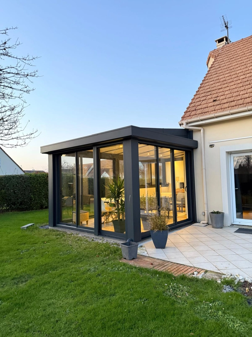 Véranda anthracite baies coulissantes, terrasse carrelée claire devant maison tuiles