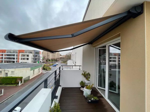 Store banne coffre toile beige, armature noire, balcon terrasse bois et garde-corps