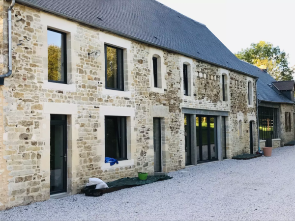 Fenêtres et portes alu anthracite sur longère en pierre claire, gravier et matériaux de chantier