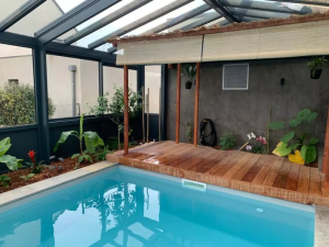 Véranda alu noir autour piscine intérieure, plage bois, kiosque paillote et plantes