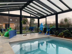 Piscine intérieure véranda noire vitrée, carrelage clair, jeux gonflables et chaises