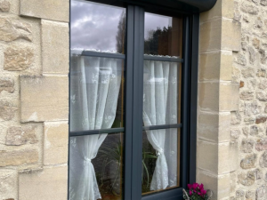 Gros plan fenetre anthracite, volet roulant, cyclamens roses sur rebord pierre