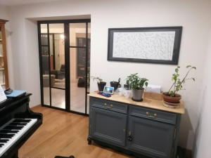 Verrière intérieure noire style atelier, piano et commode bleu près du salon