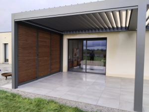 Pergola bioclimatique grise lames ouvertes, brise-vue bois coulissant et dalles