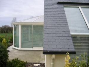 Véranda blanche vitrée adossée toiture ardoise, dalle béton sur campagne