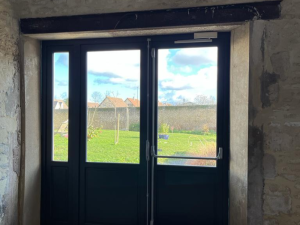 Porte vitrée anthracite barre pompier, linteau bois et jardin depuis pièce pierre