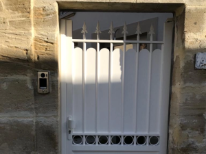 Portillon blanc fers de lance et frise ronde, mur pierre et interphone argent