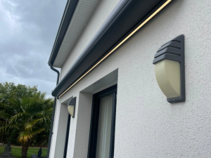 Detail coffre store anthracite, LED chaude sous appliques courbes sur mur crepi blanc