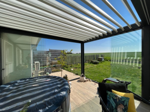 Pergola lames blanches, store zip latéral et spa gris sur terrasse bois